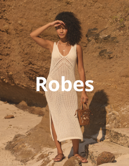 Femme portant une longue robe en crochet de la marque My Bikini Story, debout avec &eacute;l&eacute;gance sur le sable sous le soleil. 