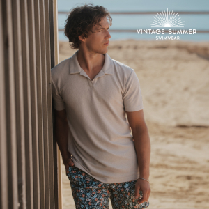 Man standing on the beach wearing a beige T-shirt paired with short swim trunks, enjoying a casual seaside moment.
